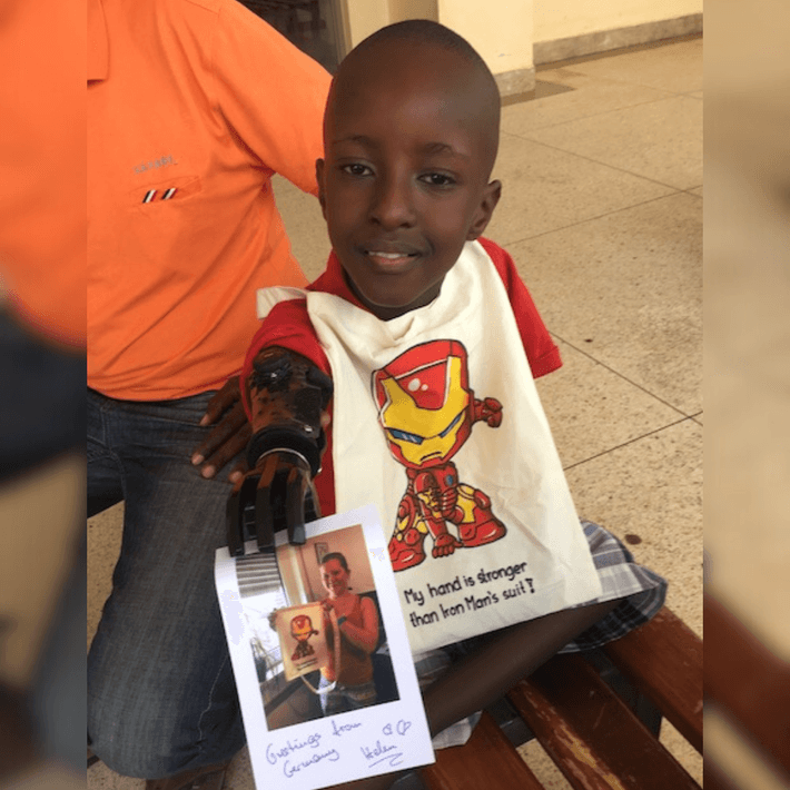 little kid holding up his letter with his new hand and his bag around his neck 