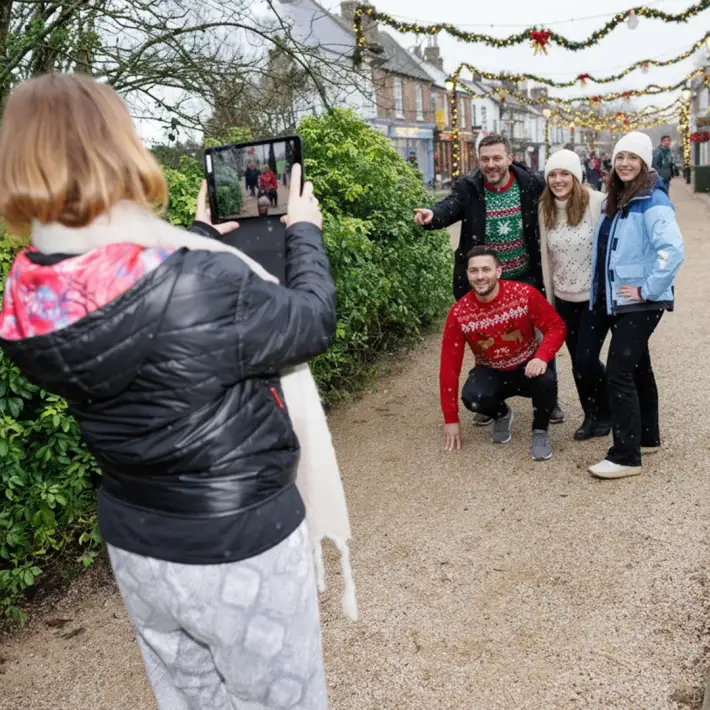 Corporate group taking part in an outdoor Christmas treasure hunt in Ireland, completing festive challenges with an iPad in a decorated town setting.