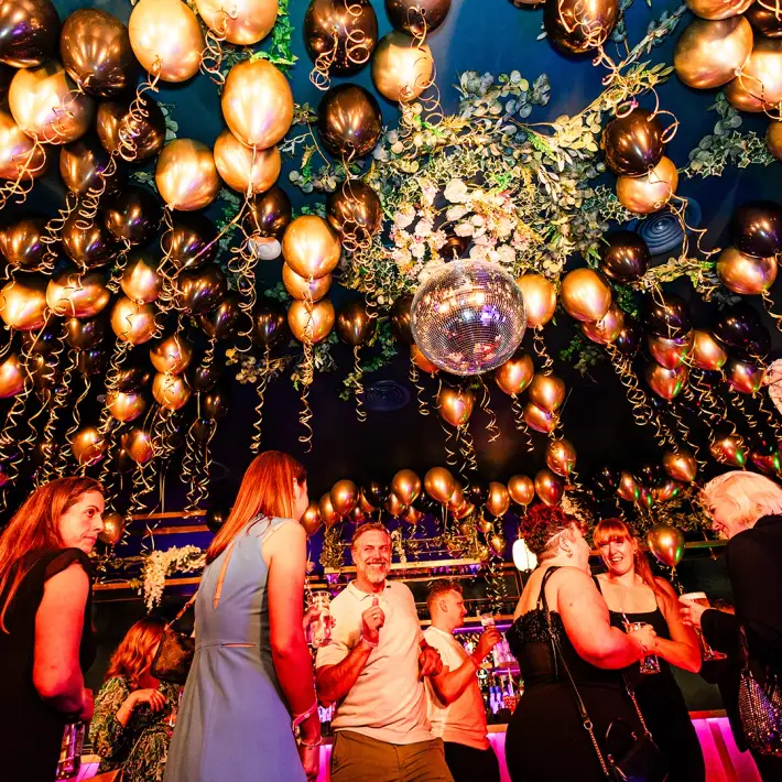 Employees dancing and socialising under gold and black balloons at a company celebration event in Dublin, Ireland.
