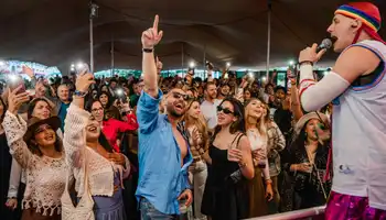 Corporate summer party with DJ playing to a crowd in front of a main stage decorated with lights and flags