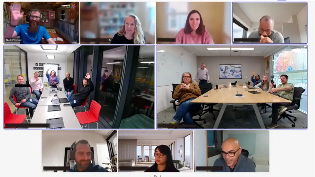 Hybrid team building activity with remote and in-office participants waving on a shared video call.