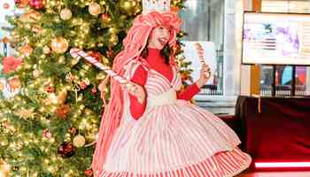 girl dressed up in Christmas outfit with a christmas tree behind her