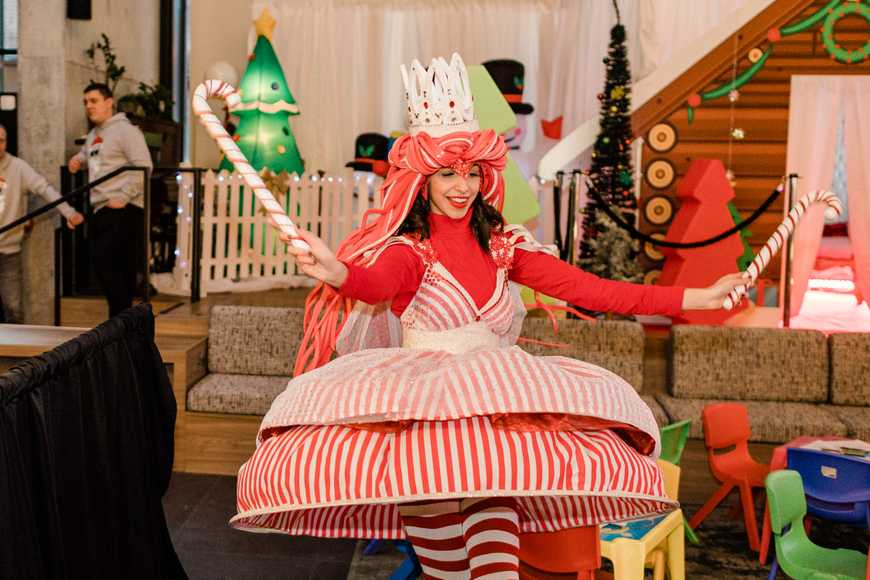 High-energy Christmas performer with candy canes dancing at a corporate Christmas team building experience with immersive festive décor.
