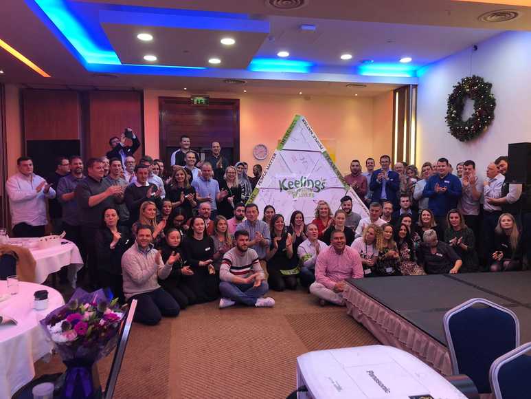 Large corporate group gathered around a giant pyramid they built together during a Pyramid Power team building activity.