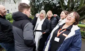Group of colleagues laughing and putting hands together during a fun outdoor team building activity in Dublin.