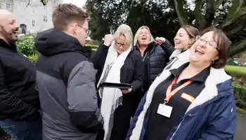 Group of colleagues laughing and putting hands together during a fun outdoor team building activity in Dublin.