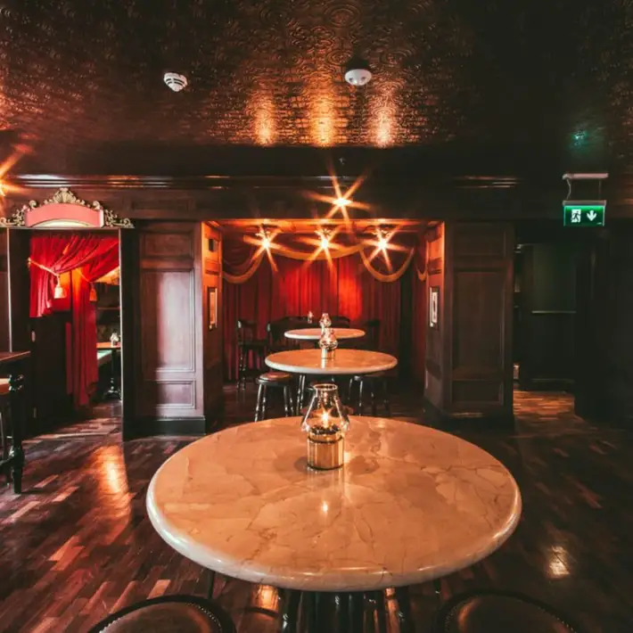 Three tall tables with lit candles infront of red curtian