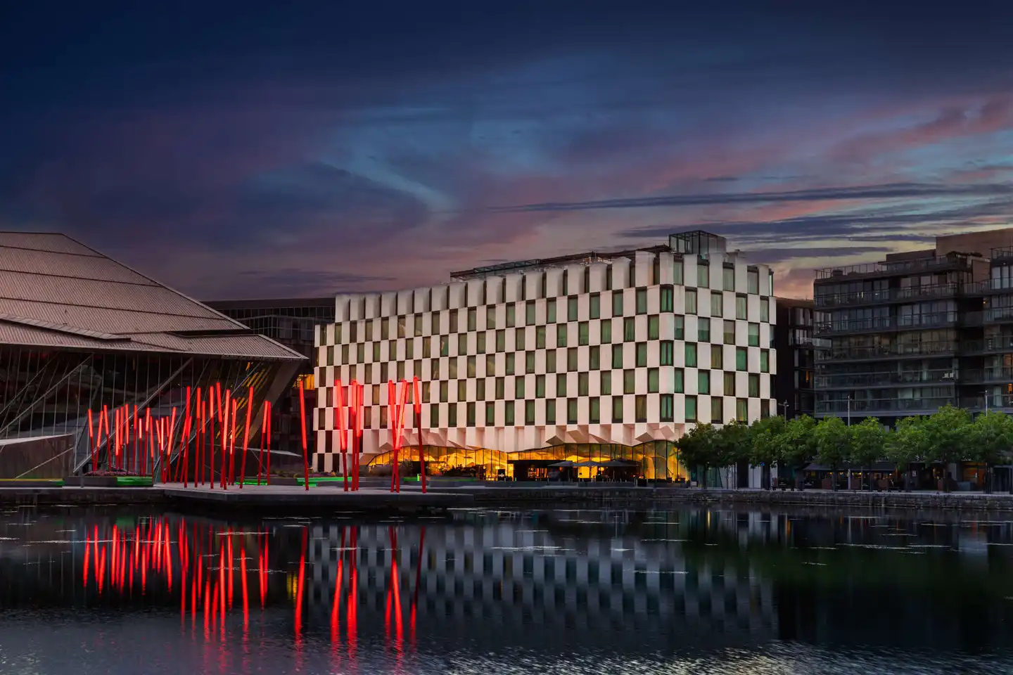 The exterior of the Anantara Hotel looking over River Liffey at night time with big red LED lights outside and the hotel is lit up for corporate events 