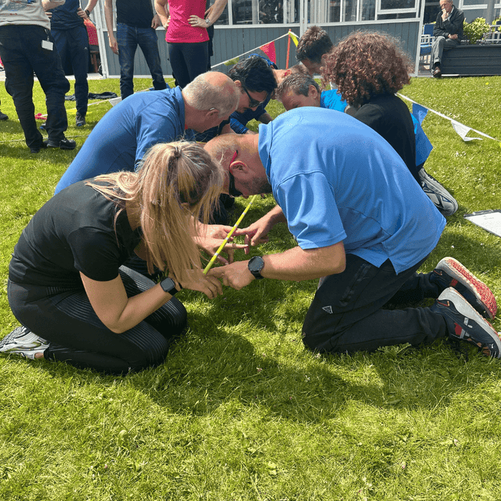 Team guiding a stick onto the ground in a straight line using their fingers only 