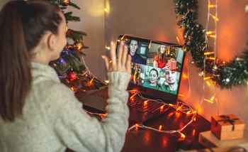 Remote employee taking part in a virtual Christmas party on a video call with festive decorations and team members on screen