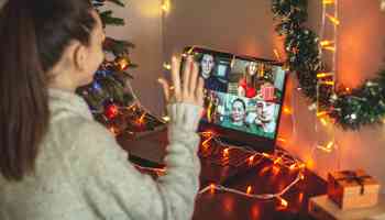 Remote employee taking part in a virtual Christmas party on a video call with festive decorations and team members on screen