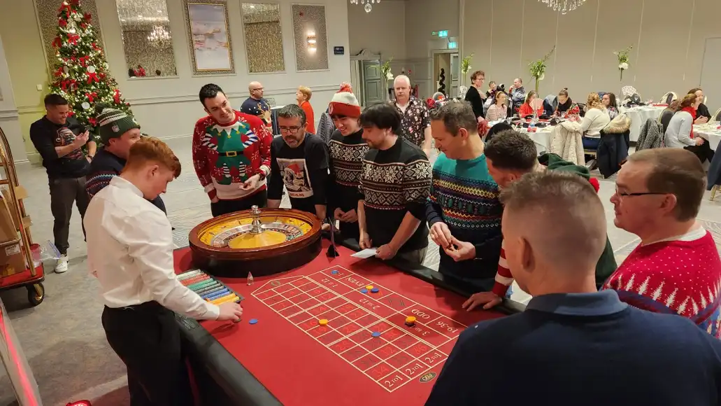 Corporate team in Christmas jumpers playing roulette at a festive casino night party with Christmas tree decorations.