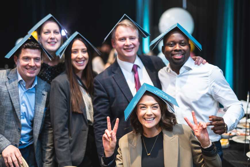 Team building group photo with branded booklets on heads, celebrating company values at a corporate event in Ireland.