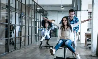 Team members laughing and racing through an office on swivel chairs during a fun indoor ice breaker activity.