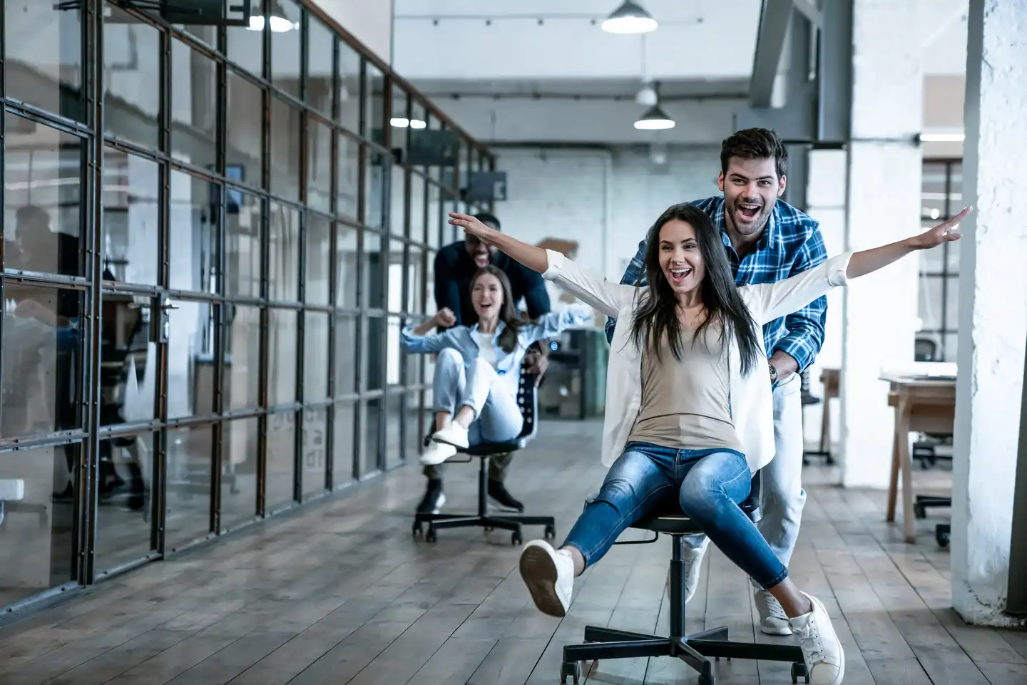 Team members laughing and racing through an office on swivel chairs during a fun indoor ice breaker activity.
