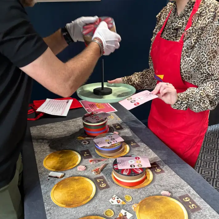 Participants in The Cake Factory team building challenge stacking cake layers with recipe cards and instructions, focusing on teamwork, problem solving, and communication.
