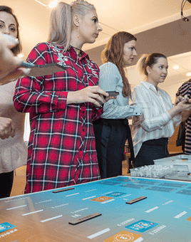 Corporate team engaged in a strategic collaboration game, analysing data on a digital tabletop during a team building workshop.