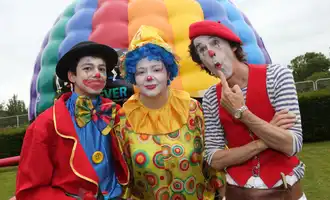 Three colourful clowns entertaining at a corporate family fun day with inflatable games in the background