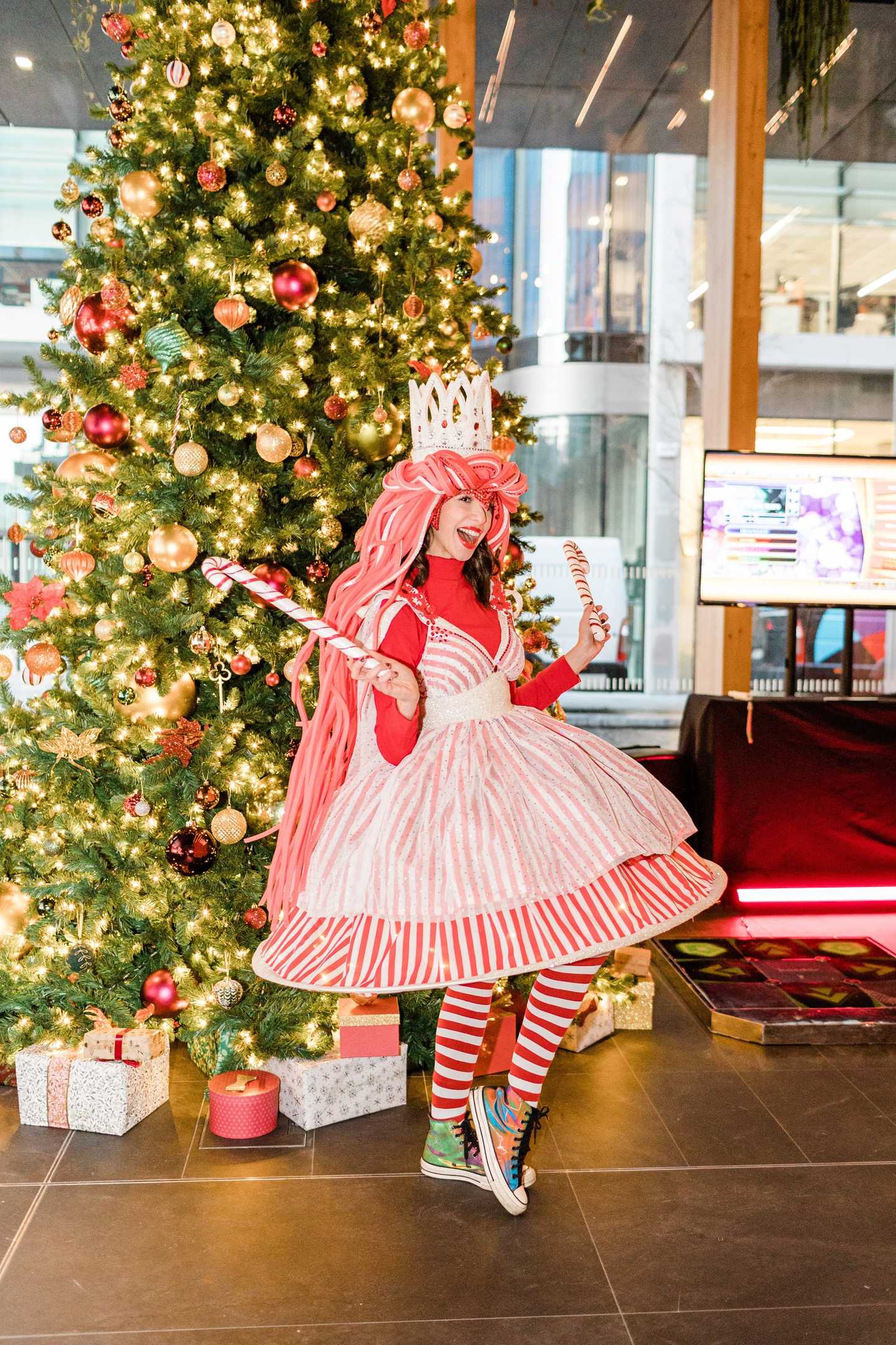 girl dressed up in Christmas outfit with a christmas tree behind her 