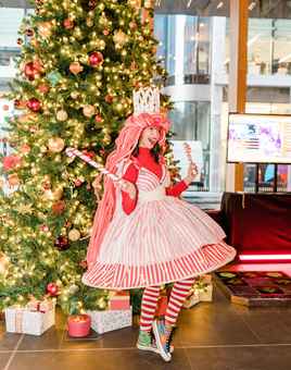 girl dressed up in Christmas outfit with a christmas tree behind her 