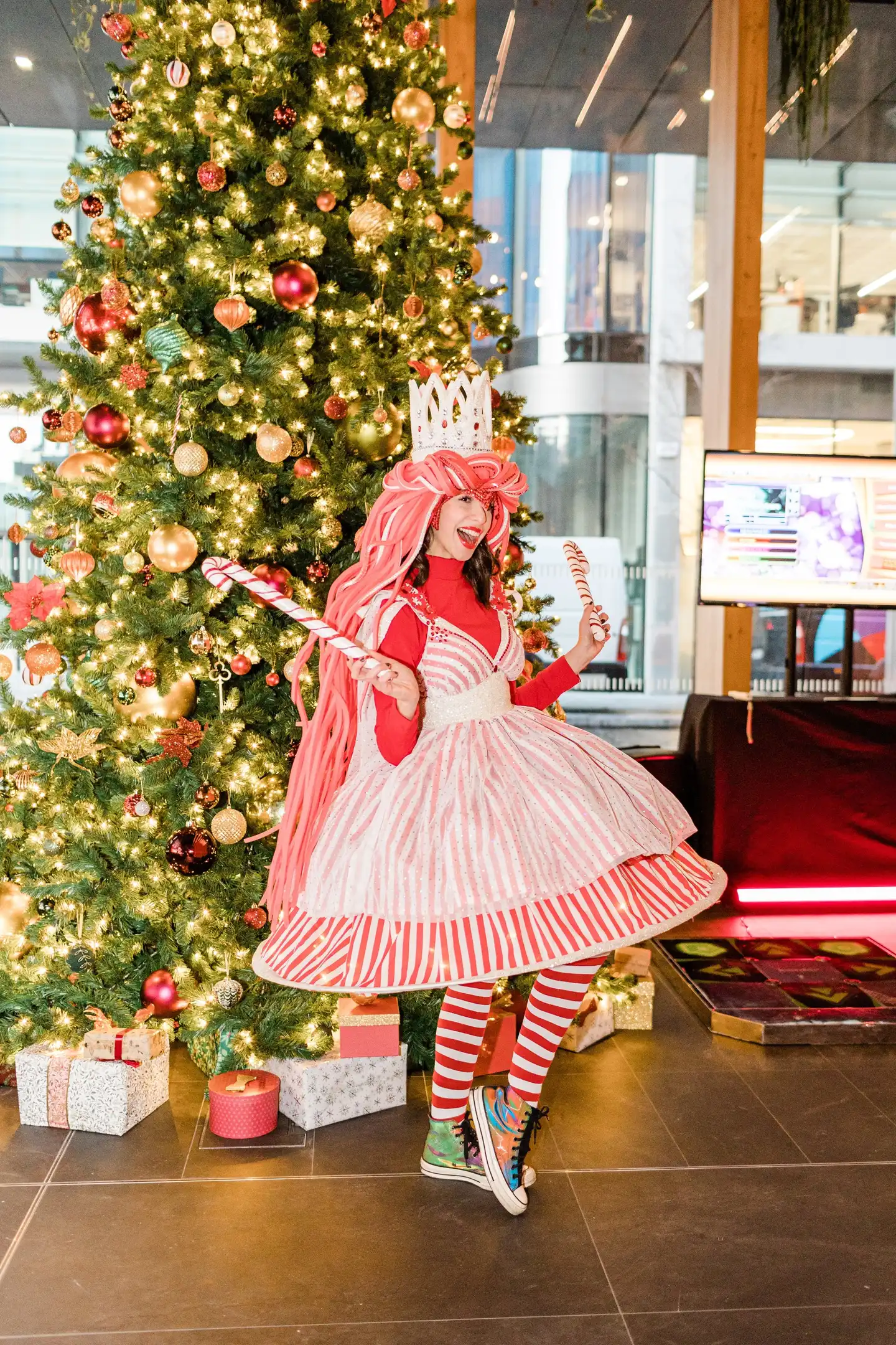 girl dressed up in Christmas outfit with a christmas tree behind her 