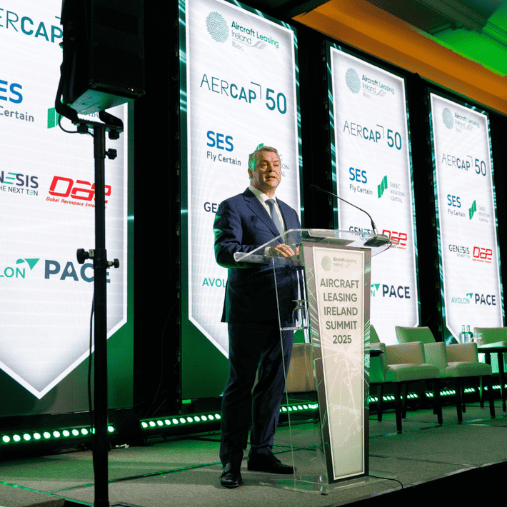 Green lights behind stage at the ALI summit with a man in a suit talking into the microphone