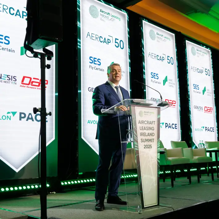 Green lights behind stage at the ALI summit with a man in a suit talking into the microphone