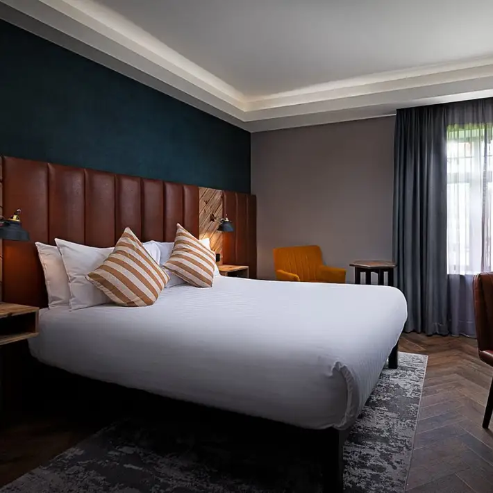 Contemporary modern bedroom with a double bed and white linen sheets, the rooms has a rustic feel due to the dark walls and timber panelling | Plan your Corporate Team-Building at Kilmurry Lodge Hotel | Dynamic Events 