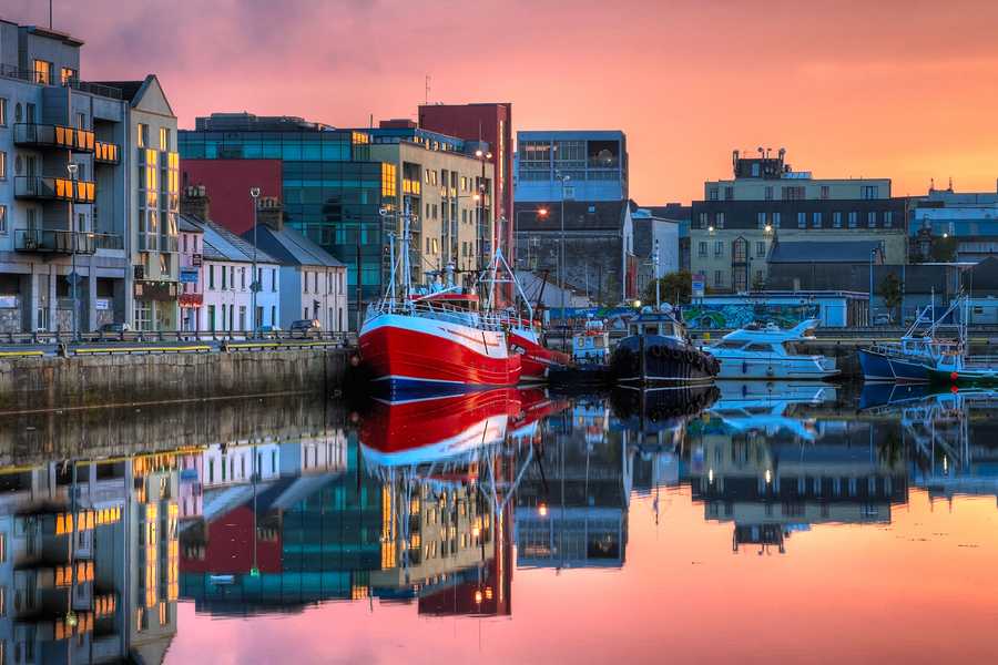 Morning sunrise over the dock with a red boat on it and a row of houses | Event Management Galway