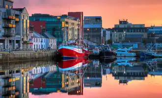 Morning sunrise over the dock with a red boat on it and a row of houses | Event Management Galway