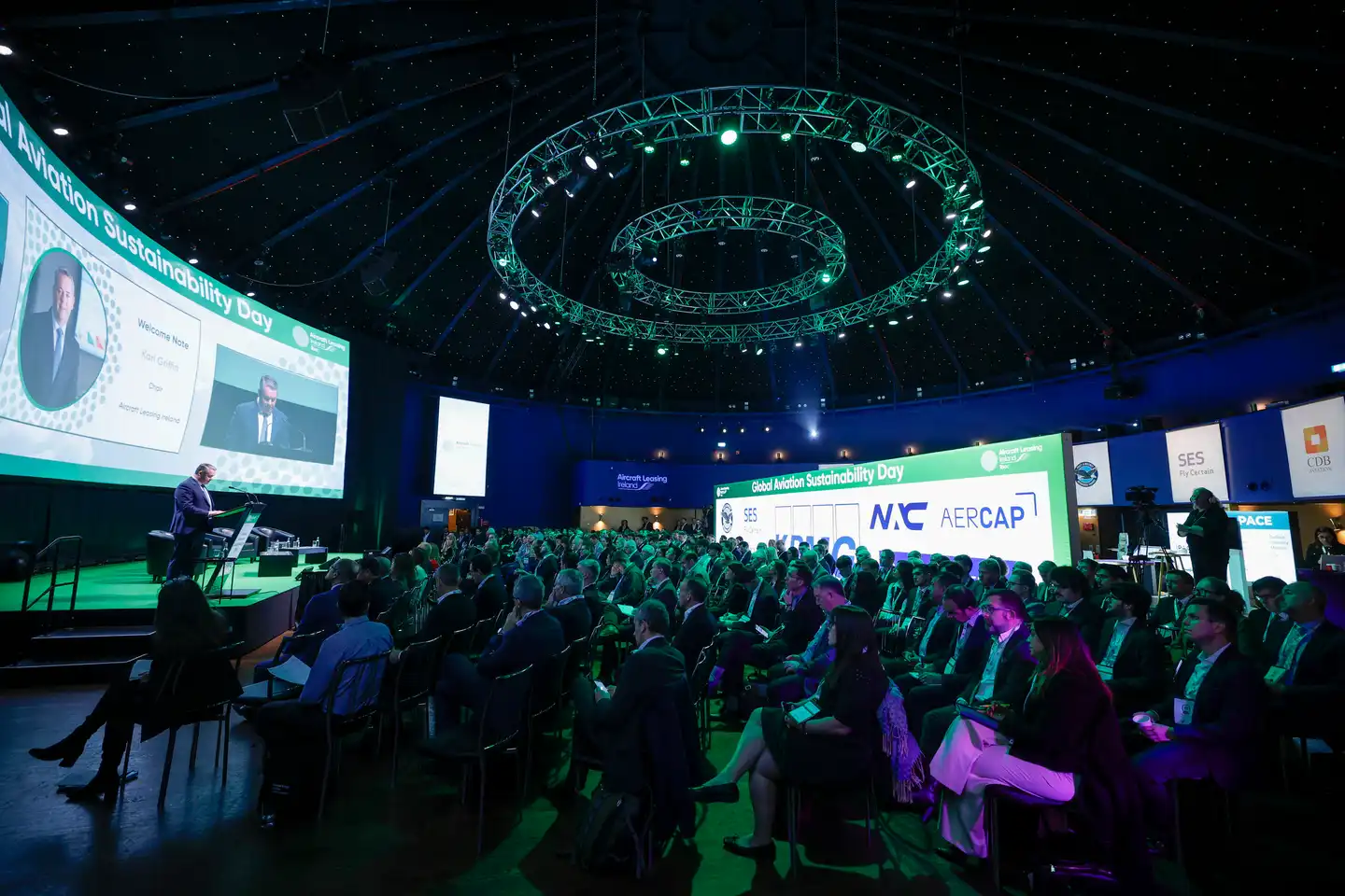 Large audience attending a company kick-off conference in Ireland with keynote speaker on stage, branded screens, and professional event setup by Dynamic Events.