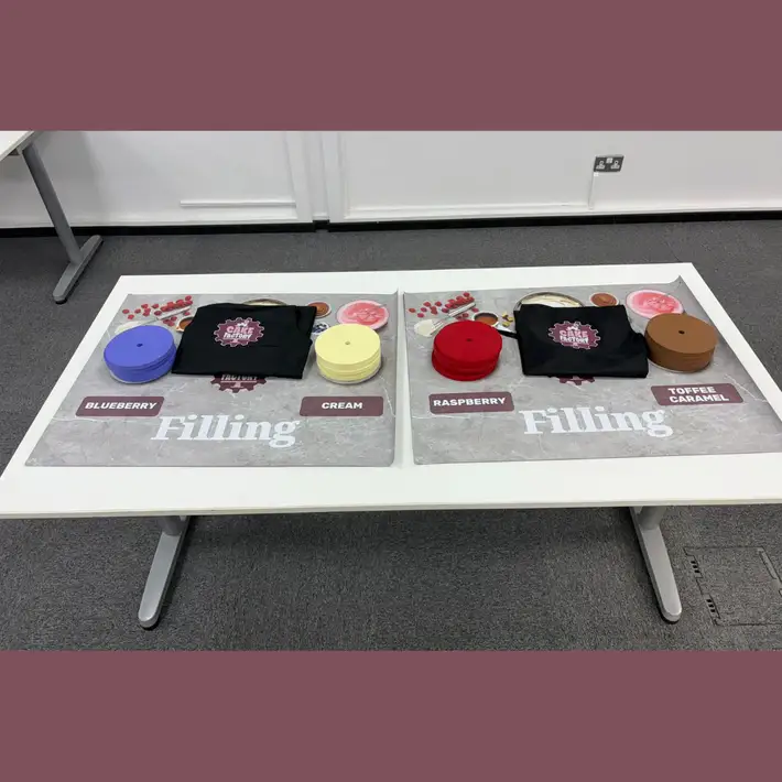 Close-up of a production station showing baking trays, recipe cards, and time-tracking sheets used during the simulation.