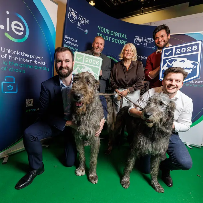 Exhibitors posing with two Irish Wolfhounds at the Digital Trust exhibition stand during the NCSC Cyber Expo in Dublin.