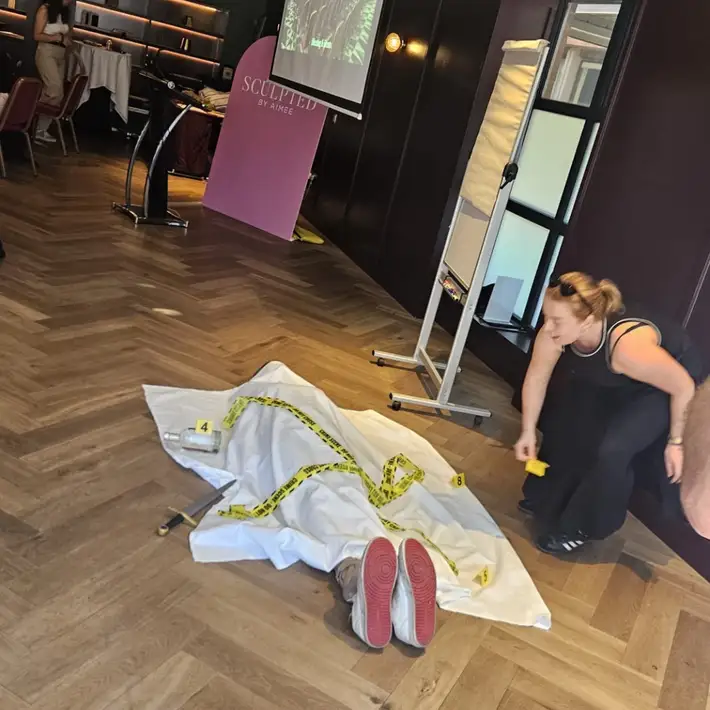 the set up of the crime scene with an actor on the ground and a sheet over the body with yellow caution tape around it 