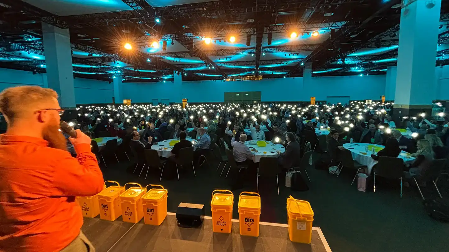Corporate team in Ireland taking part in a SolarBuddy CSR team building event, holding assembled solar lights during the Hour of Power activity in a large conference venue.