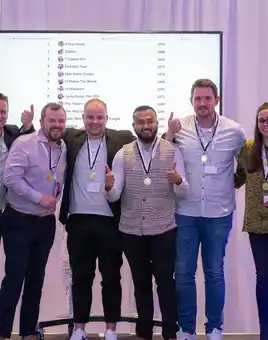Corporate quiz winners posing with medals in front of live team scoreboard during team building event in Ireland