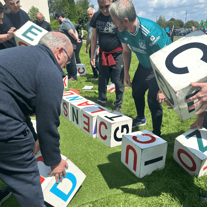 Team members arranging large alpha blocks to solve a word challenge during an outdoor team-building exercise.
