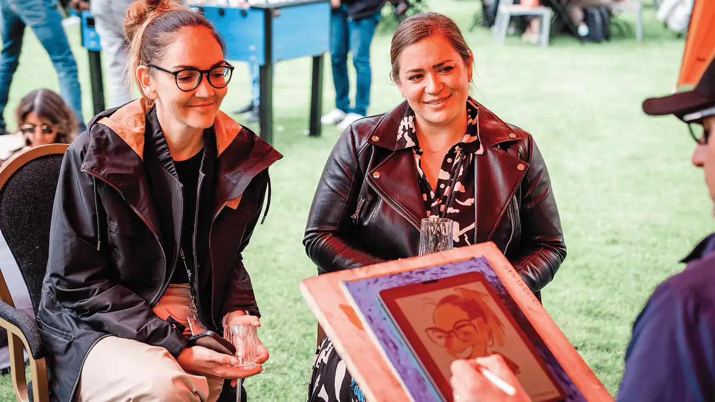 corporate team building caricature activity with two colleagues laughing while live caricature artist draws them at outdoor company event in Ireland