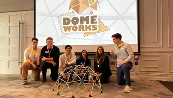 Group of graduates with the fastest time building a domeworks posing in front of the structure with medals and a Domeworks team training backdrop