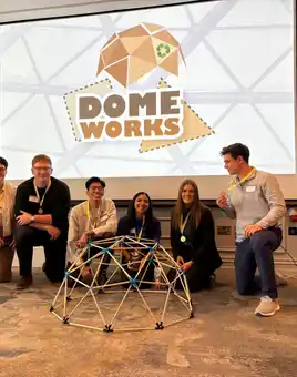 Group of graduates with the fastest time building a domeworks posing in front of the structure with medals and a Domeworks team training backdrop