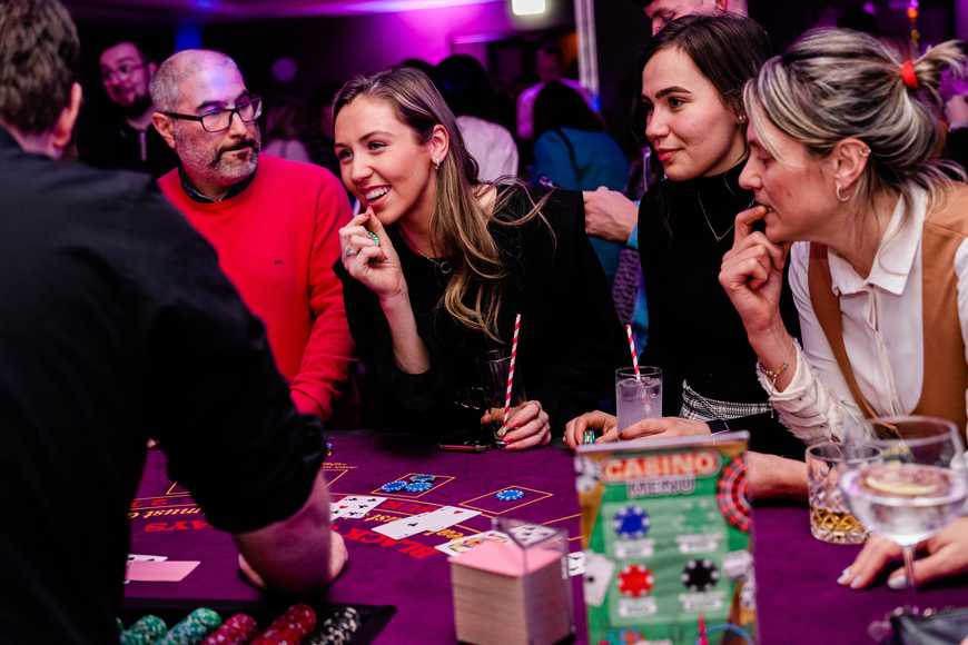 Group of colleagues smiling and playing blackjack at a festive corporate casino night Christmas party.