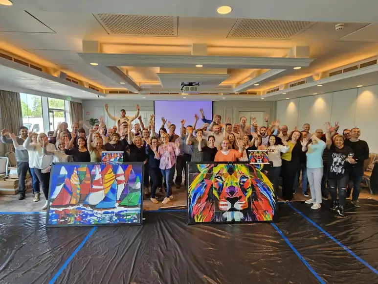 Corporate team building group in Ireland celebrating after completing Big Picture art workshop with collaborative paintings of a lion and sailing boats.