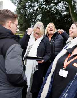 Group of colleagues laughing and putting hands together during a fun outdoor team building activity in Dublin.