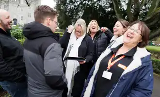 Group of colleagues laughing and putting hands together during a fun outdoor team building activity in Dublin.