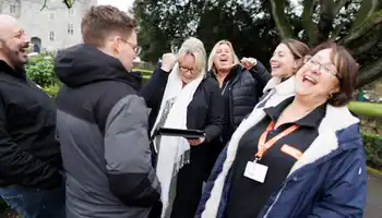 Group of colleagues laughing and putting hands together during a fun outdoor team building activity in Dublin.