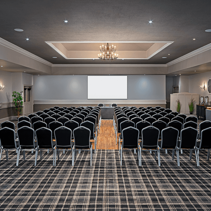 Elegant conference room setup with rows of black chairs facing a large projector screen, under a stylish chandelier at Kilmurry Lodge Hotel | Plan your Corporate Team-Building at Kilmurry Lodge Hotel | Dynamic Events
