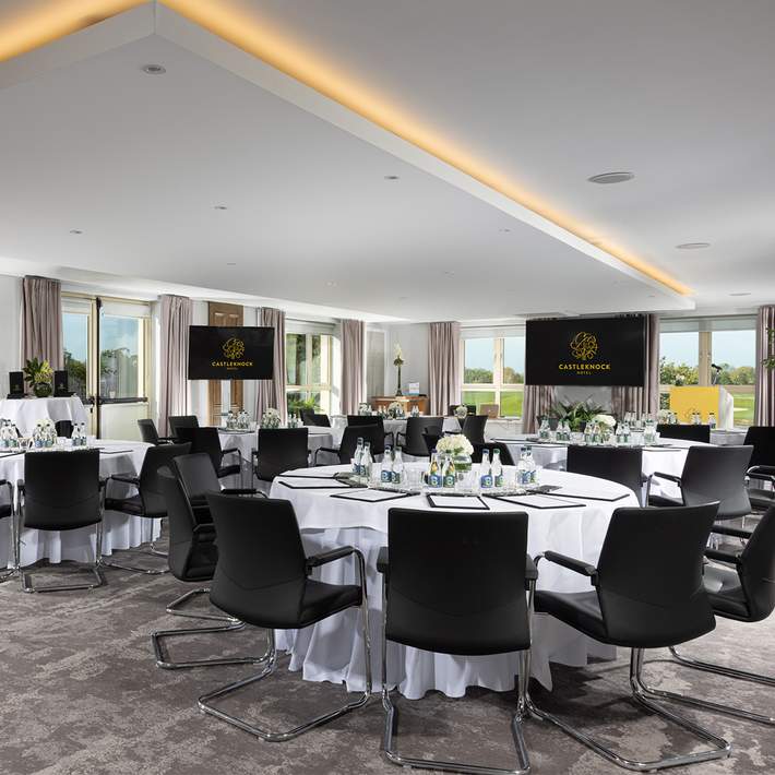 Premium conference venue at Castleknock Hotel, Dublin, featuring a spacious layout with round tables, gold-trimmed chairs, and a professional AV setup—perfect for corporate meetings, networking events, and business conferences. Managed by Dynamic Events Ireland.