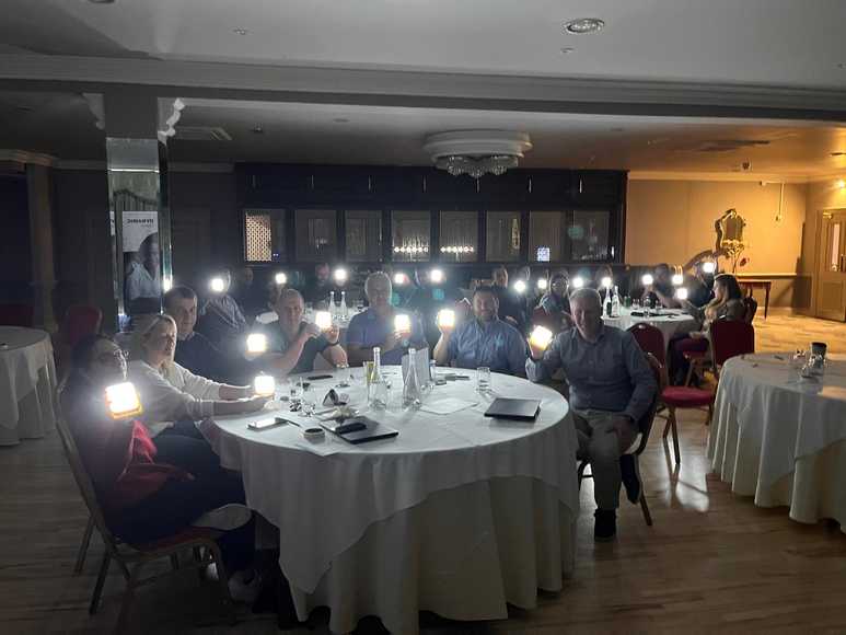 Group sitting at round tables assembling SolarBuddy lights at CSR corporate event