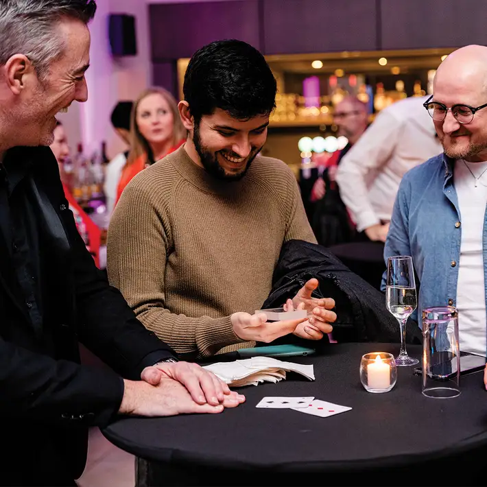 Corporate team building magic workshop with participants learning and performing a close-up card trick in a group setting
