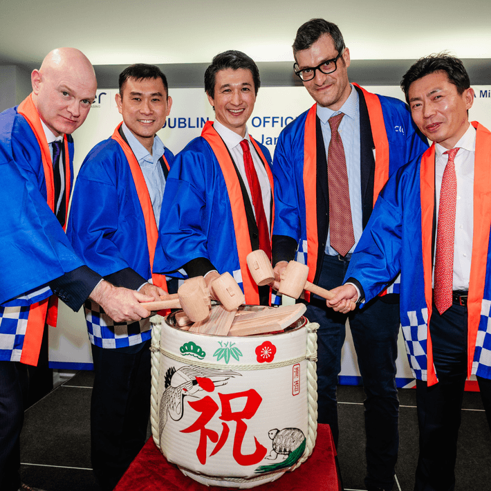 Business leaders wearing traditional happi jackets participate in a Japanese sake barrel ceremony at a corporate launch event in Dublin, celebrating the opening of a new office.